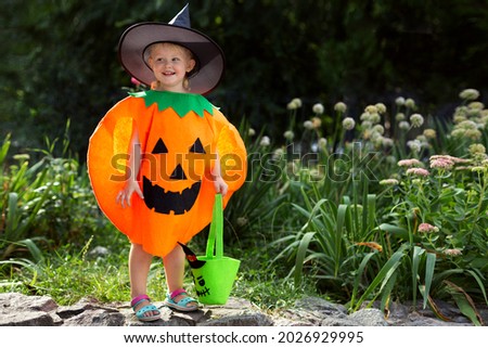 Little smiling girl in a pumpkin costume and with a bag for sweets on the street. A beautiful girl will celebrate Halloween. The concept of Halloween