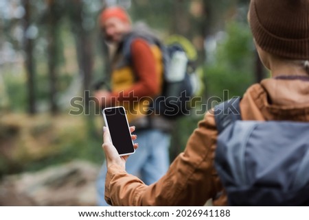 woman holding smartphone while blank screen near blurred man in forest 