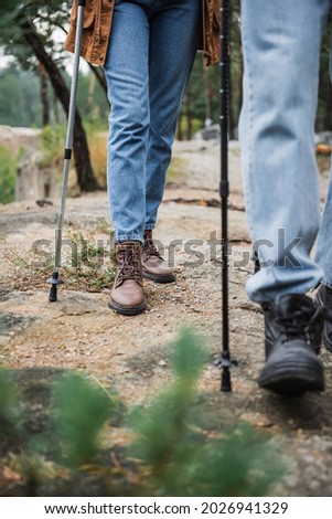 cropped view of young couple walking with hiking sticks on rocky ground 