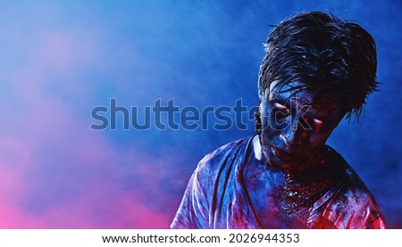 Portrait of a scary zombie boy teenager in blue and crimson smoky lighting. Halloween, horror movie.  Royalty-Free Stock Photo #2026944353