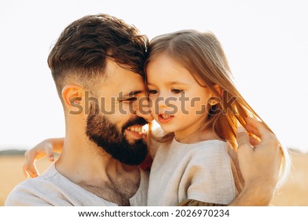 Cute little daughter in his fathers arms. Dad and daughter having fun on sunny summer day in park. Adorable child being held by his daddy
