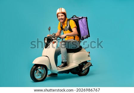 Young courier, delivery man in uniform with thermo backpack on a moped isolated on blue background. Fast transport express home delivery. Online order. Royalty-Free Stock Photo #2026986767