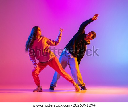 Smooth movements. Two young people, guy and girl, dancing contemporary dance over pink background in neon light. Modern dance aesthetics concept