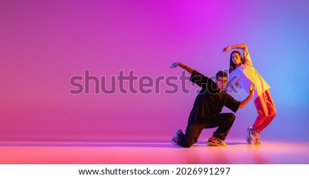 Flyer. Strange body movements. Two young people, guy and girl dancing contemporary dance over pink background in neon light. Modern dance aesthetics concept Royalty-Free Stock Photo #2026991297