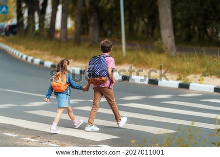 girl and boy with backpacks carefully cross road on pedestrian crossing on their way to school. Traffic rules. Walking path along zebra in city. concept of pedestrians crossing pedestrian crossing. Royalty-Free Stock Photo #2027011001