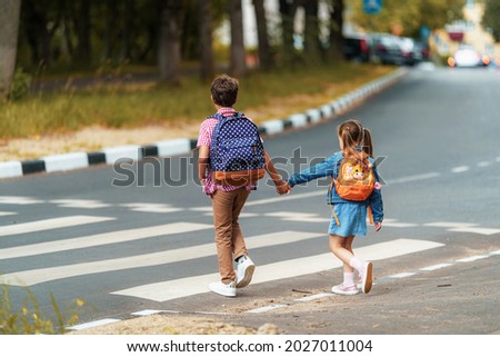 girl and boy with backpacks carefully cross road on pedestrian crossing on their way to school. Traffic rules. Walking path along zebra in city. concept of pedestrians crossing pedestrian crossing. Royalty-Free Stock Photo #2027011004