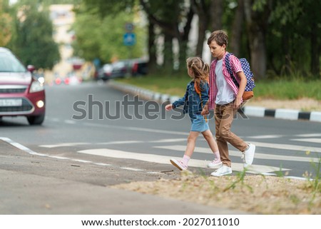 girl and boy with backpacks carefully cross road on pedestrian crossing on their way to school. Traffic rules. Walking path along zebra in city. concept of pedestrians crossing pedestrian crossing.