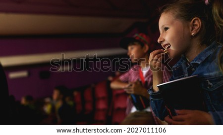 Portrait happy children grabbing popcorn from bucket while watching movie at cinema. child looks interested and emotionally excited. Happy childhood. Leisure, fun pastime, hobby emotions. Copy space