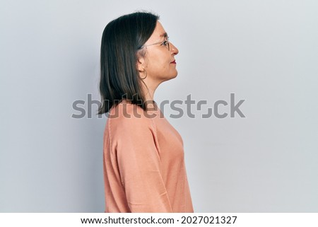 Middle age hispanic woman wearing casual clothes and glasses looking to side, relax profile pose with natural face with confident smile. 