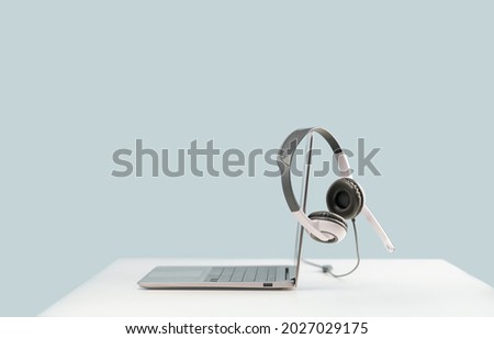 Side view of slim laptop with headphones headset on white desk. Blue background. Distant learning. working from home, online courses or support. Audio podcast. Helpdesk or call center. Side view