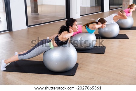 Adult sports people practiciting Pilates in the studio during a group training session perform an exercise on a fitness ball, ..which strengthens the lumbar region and develops overall flexibility Royalty-Free Stock Photo #2027065361