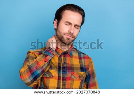Photo of upset unhappy young man wear plaid shirt arm neck feeling tired isolated blue color background
