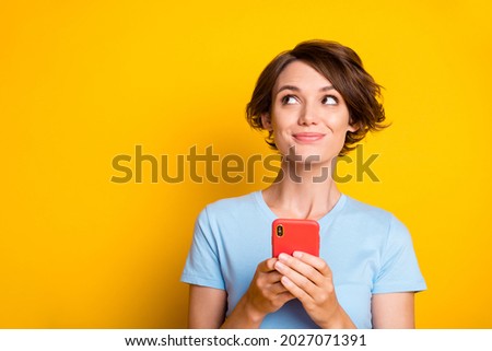 Photo of young attractive girl happy smile dream dreamy look empty space use smartphone isolated over yellow color background