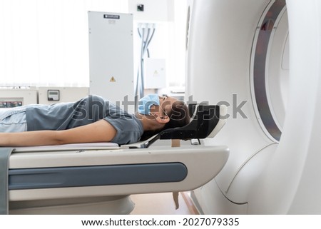 A woman in a medical mask lies on the tomograph table. woman is undergoing computed axial tomography examination in a modern hospital Royalty-Free Stock Photo #2027079335