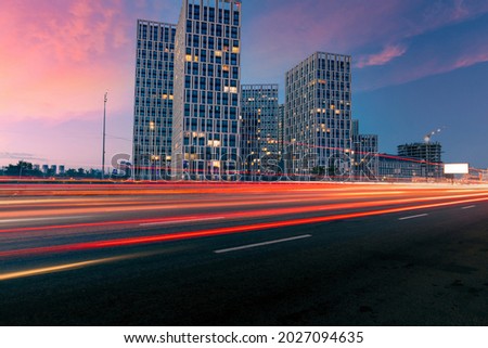 Dusk city street. Lights trails from moving cars on the evening highway with a group of modern buildings on the opposite side.