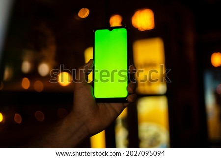 hand holding cell phone with screen on camera in the city at night with car lights in background