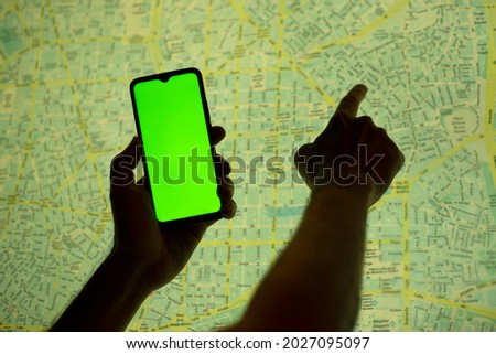 
hand holding a cell phone with the screen on camera and the other hand pointing to a map of the city