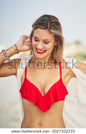 Cheerful woman on beach touching her hair and smiling