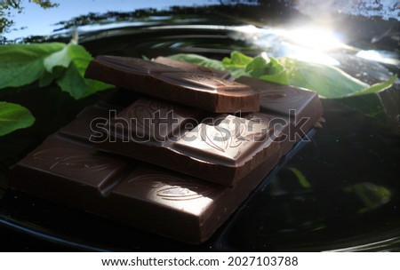 New picture with dark bitter chocolate with mint on luxury black glass plate and fresh green leaves of mint in sun lights 