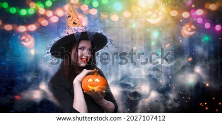 Portrait of happy smiling witch with glowing carved pumpkin on festive forest background with magic lights.Beautiful young woman in witch costume with cloack and orange hat.Halloween party art design 