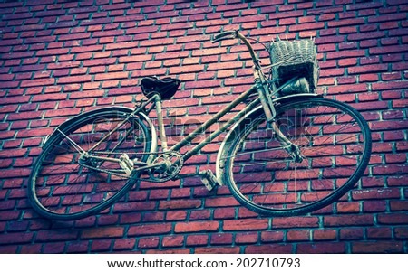 Old rusty bike attached to red brick wall. Aged photo.