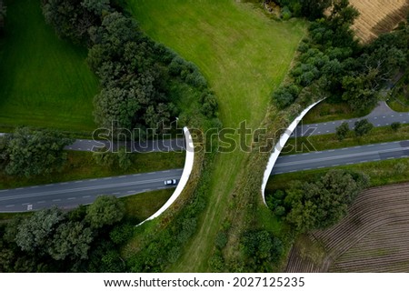 Road traversed by wildlife crossing forming a safe natural corridor bridge for animals to migrate between conservancy areas. Environment nature reserve infrastructure eco passage. Royalty-Free Stock Photo #2027125235