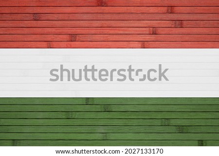 The national state flag of Hungary painted on the background of a wooden wall made of bamboo.