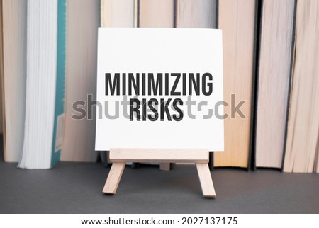 White card with text minimizing risks stands on the desk against the background of books stacked