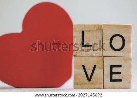 Vibrant red wooden love heart on display with small letter tiles spelling the word LOVE. White background with copy space.