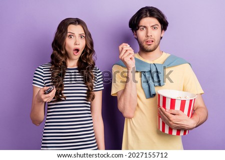 Photo of shocked excited couple wear casual clothes 3d spectacles holding tv remote eating pop corn isolated violet color background