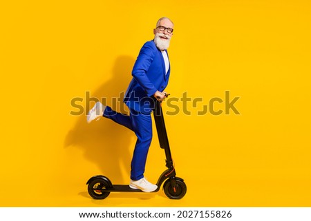 Full body profile photo of funny grey beard aged man ride scooter wear spectacles blue suit isolated on yellow background
