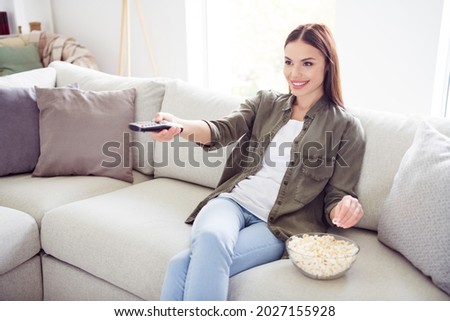 Photo of sweet charming young lady wear green shirt smiling eating pop corn changing channels indoors room home