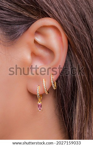 Woman ear with mulriple piercings wearing beautiful earrings with zirconia- details capture Royalty-Free Stock Photo #2027159033
