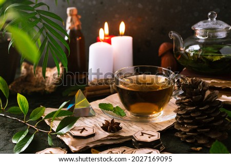Wooden runes are lying on the table among the papers with notes. There is a mug of tea next to it. Astrology and esotericism. Royalty-Free Stock Photo #2027169095