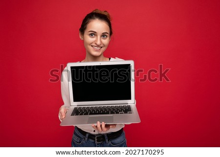 Photo of beautiful young woman holding computer laptop looking at camera isolated over colourful background