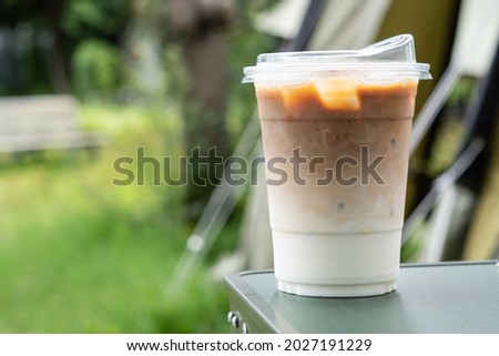 showing a glass cup of ice coffee latte outdoors on green leaf background