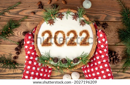 Festive cake with the numbers 2022 on white cream, decorated with cones, coniferous branches and star anise. Concept of the New Year.