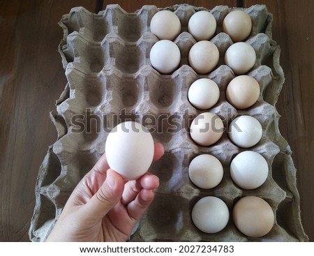 Woman's hand picking egg from egg tray on wooden table. Hand-selected egg in brown paper trays containers. a lot of egg shells in the background, bio-organic produce, eco food concept. blurry, so grai