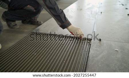 Installing a large ceramic tile. Workers lay large tiles on the floor. Royalty-Free Stock Photo #2027255447