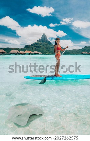 SUP Stand-up paddle board woman wwimming with stingrays tourist tour activity happy Asian woman on Bora Bora island beach at Tahiti overwater bungalow hotel, holiday travel vacation. Royalty-Free Stock Photo #2027262575