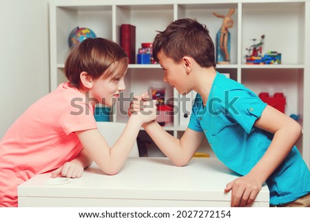 Classmates competing in arm wrestling during the break. Happy friends playing arm wrestle looking at each other. Handshake of children. Students having fun at classroom.