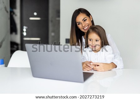 Beautiful mother and child looks at laptop screen spend time in kitchen using app education program, choose cartoons, teach kid pc usage, controls what daughter watching on internet cyberspace concept