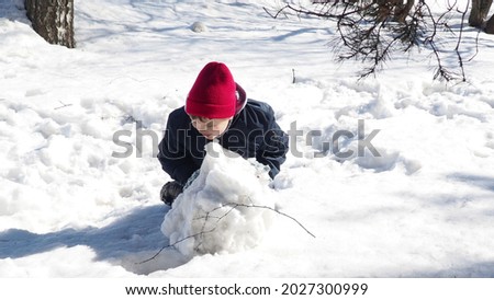 Little boy in red winter hat and clothes having fun with snowman. Active outdoors leisure with children in winter. Kid during stroll in a snowy winter park