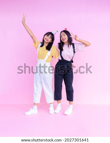 Two happy young girl standing on pink background.