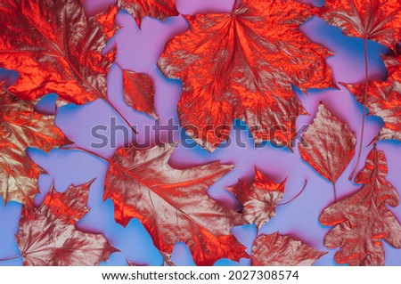 Pattern of dry orange metallic leaves on violet background with neon light. Autumn natural concept. Top view, flat lay.