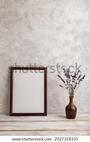 Brown wooden frame mockup with lavender in ceramic vase on gray concrete background. Blank, vertical orientation, still life, copy space.