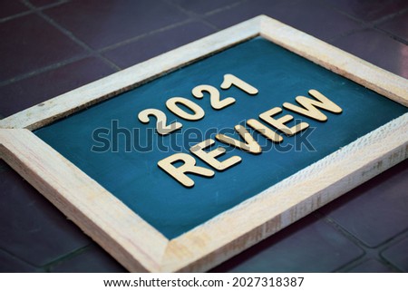 A chalkboard with the message 2021 REVIEW written in 3d wooden alphabet letters laid on dark background. 