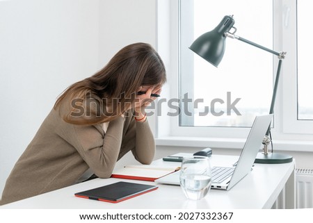 Attractive caucasian woman graphic designer tired of hard work. Sad girl cover face with hands. On table laptop, graphic tablet, glass of water and notepad. Female horrified by the number of tasks.