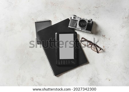 E-reader, notebooks, photo camera and eyeglasses on light background