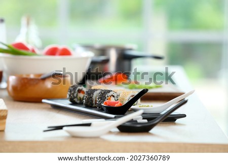 Plate with tasty sushi rolls on table in kitchen